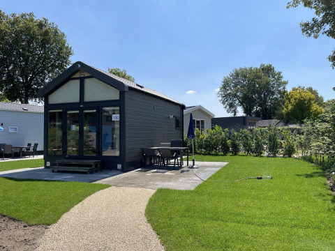Moderne tiny house ved Holiday park Ackersate i Holland med grøn have, terrasse og spisebord udenfor.