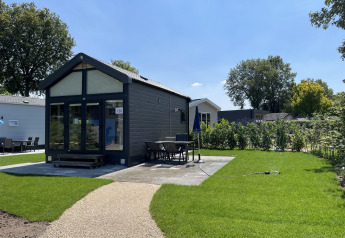 Moderne tiny house ved Holiday park Ackersate i Holland med grøn have, terrasse og spisebord udenfor.