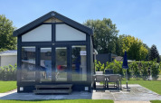 Lille hus ved Holiday park Ackersate i Holland, med glasfacade, terrasse og havemøbler på solrig dag.