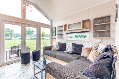 Lichte, moderne zithoek van tiny house bij Holiday park Ackersate, met grote ramen en zicht op grasveld.