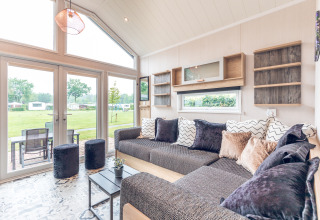 Lichte, moderne zithoek van tiny house bij Holiday park Ackersate, met grote ramen en zicht op grasveld.