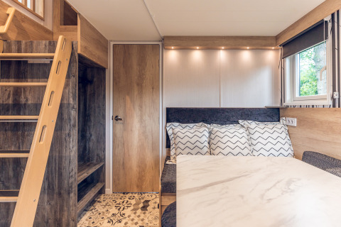 Modern, cozy tiny house interior at Holiday Park Ackersate with ladder, door, table, pillows, and window.
