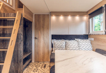 Modern, cozy tiny house interior at Holiday Park Ackersate with ladder, door, table, pillows, and window.