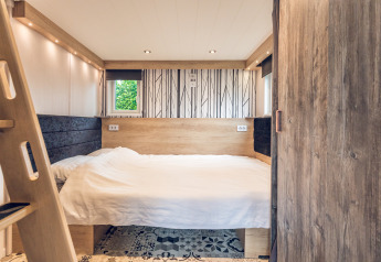 Camera da letto tiny house a Holiday Park Ackersate, Paesi Bassi, con arredo in legno e letto matrimoniale.