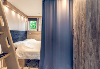 Schlafbereich in einem Tiny House im Holiday Park Ackersate, Niederlande, mit Bett, Vorhang und Leiter.