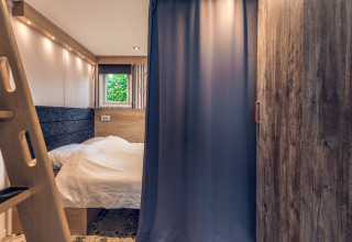 Dormitorio acogedor en una tiny house del Holiday Park Ackersate, Países Bajos, con cama y cortina.