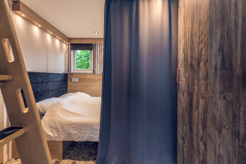 Knusse slaapkamer in een tiny house bij Vakantiepark Ackersate, Nederland, met bed, gordijn en raam.