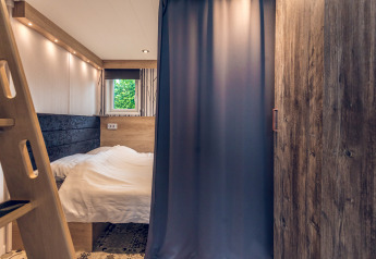 Camera da letto in una tiny house all’Holiday Park Ackersate nei Paesi Bassi, con letto e tenda.