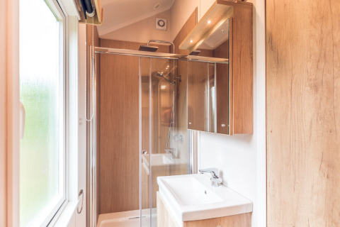Baño moderno con detalles en madera, cabina de ducha y ventana en una tiny house en Holiday park Ackersate.