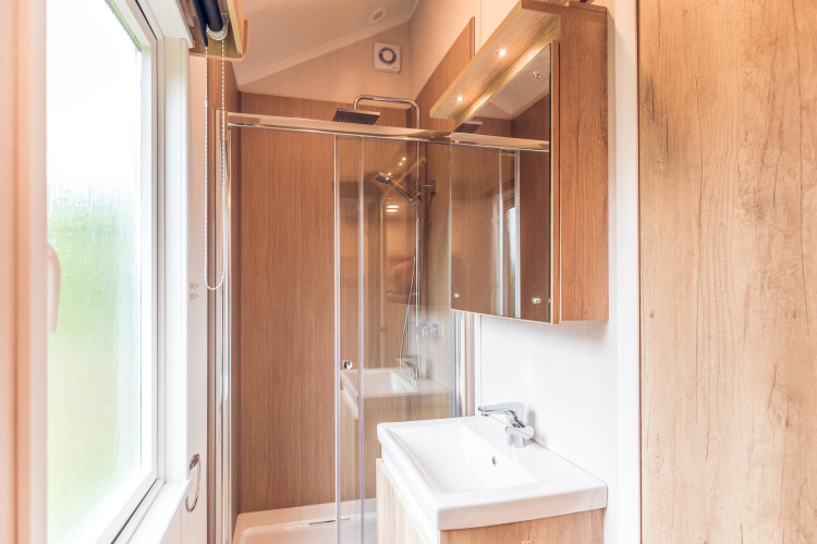 Modern bathroom with wood accents, shower enclosure and window in a tiny house at Holiday park Ackersate.