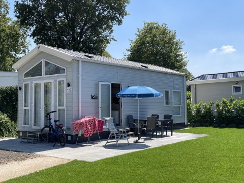 Tiny house with patio, umbrella, outdoor dining set, and bike at Holiday park Ackersate in the Netherlands.