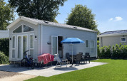 Casa pequeña con patio, sombrilla y bicicleta en Holiday park Ackersate, Países Bajos, día soleado.
