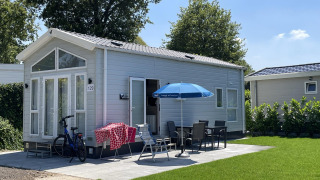 Tiny house with patio, umbrella, outdoor dining set, and bike at Holiday park Ackersate in the Netherlands.