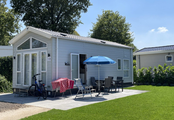 Casa piccola con terrazza, mobili da giardino e bici al Holiday park Ackersate nei Paesi Bassi, giorno di sole.