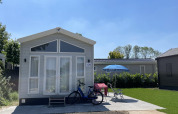 Tiny house at Holiday park Ackersate in the Netherlands with a bike, chairs, and umbrella in front.