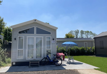 Pequeña casa en Holiday park Ackersate en los Países Bajos con bici, sillas y paraguas al frente.