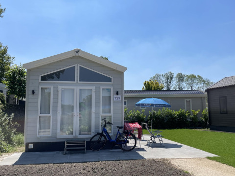 Tiny house at Holiday park Ackersate in the Netherlands with a bike, chairs, and umbrella in front.