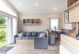 Lichte en moderne woonkamer in een tiny house op Holiday park Ackersate, Nederland, met grijze zetel.