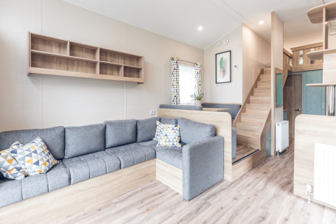 Moderne og lys stue i et tiny house på Holiday park Ackersate, med grå sofa og trappe til hems.