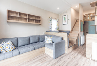 Lichte, moderne woonkamer in een tiny house bij Holiday park Ackersate, met grijze zetel en bovenverdieping.