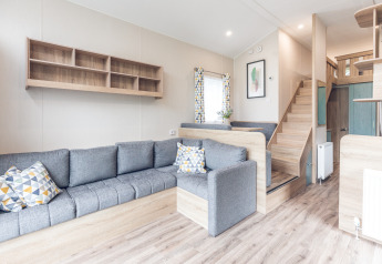 Moderne og lys stue i et tiny house på Holiday park Ackersate, med grå sofa og trappe til hems.