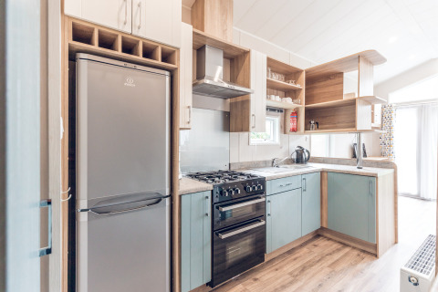 Cucina moderna e compatta con frigorifero, forno e scaffali in legno in un piccolo lodge nei Paesi Bassi.