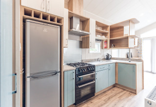 Moderne lille køkken med lyse skabe, køleskab, ovn og åbne hylder i en lille lodge i Holland.