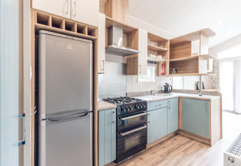 Modernes, kompaktes Kücheninterieur mit Kühlschrank, Ofen und Holzregalen in einer Lodge in den Niederlanden.