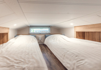 Low ceiling loft with two single beds and wood paneling in Tiny house at Holiday park Ackersate, Netherlands.