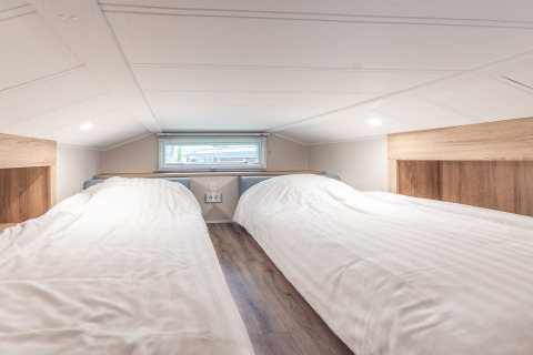 Low ceiling loft with two single beds and wood paneling in Tiny house at Holiday park Ackersate, Netherlands.
