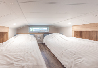 Soppalco dal soffitto basso con due letti singoli al Tiny house di Holiday park Ackersate, Paesi Bassi.