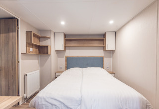 Bedroom inside a tiny house at Holiday park Ackersate in the Netherlands, featuring a double bed and shelves.