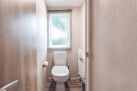 Piccolo bagno con finestra, WC e termosifone in una lodge a Holiday park Ackersate, Paesi Bassi.