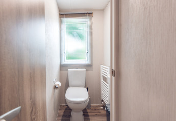Compact bathroom with window, toilet, and radiator in a lodge at Holiday park Ackersate, Netherlands.