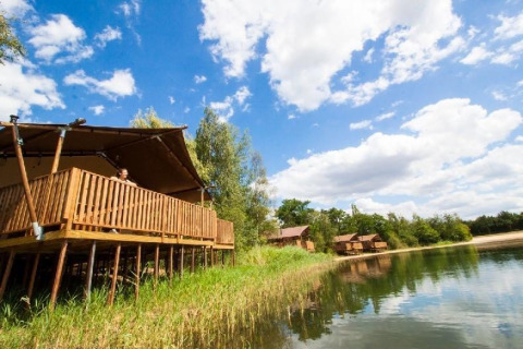 Wasser-Lodge im Ferienpark BreeBronne, Niederlande, auf Stelzen am See unter blauem Himmel.
