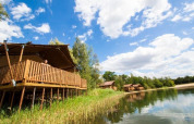 Cabaña Water Lodge en Holiday Park BreeBronne, Países Bajos, junto a un lago y cielo azul con nubes.