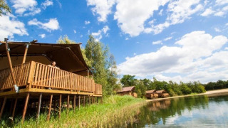 Wasser-Lodge im Ferienpark BreeBronne, Niederlande, auf Stelzen am See unter blauem Himmel.