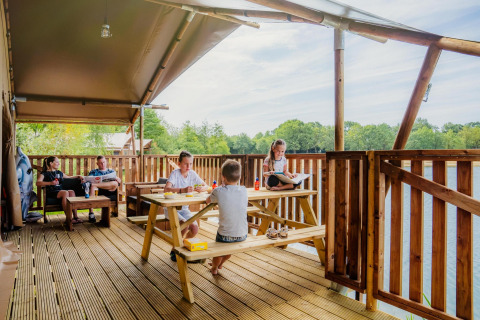 Familie entspannt sich und genießt Essen auf der Terrasse der Water Lodge WL im Holiday Park BreeBronne.