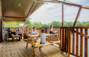 Familie entspannt sich und genießt Essen auf der Terrasse der Water Lodge WL im Holiday Park BreeBronne.