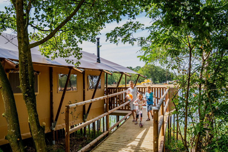Familia camina por sendero de madera junto a la Water Lodge WL en Holiday Park BreeBronne, Países Bajos.
