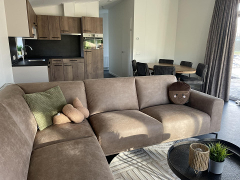 Moderne woonkamer en keuken in Wood Cottage, Holiday park De Witte Berg met bruine zetel en eettafel.