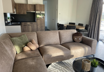 Moderne stue og køkken i Wood Cottage, Holiday park De Witte Berg, med brun sofa og spisebord.