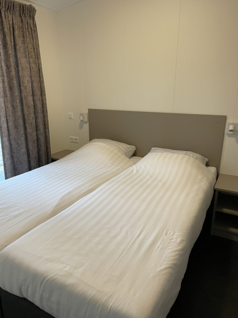 Dos camas individuales con sábanas blancas en una cabaña Wood Cottage en Holiday park De Witte Berg, Países Bajos.