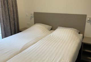 Dos camas individuales con sábanas blancas en una cabaña Wood Cottage en Holiday park De Witte Berg, Países Bajos.