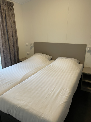 Zwei Einzelbetten mit weißer Bettwäsche im Wood Cottage im Ferienpark De Witte Berg, Niederlande.