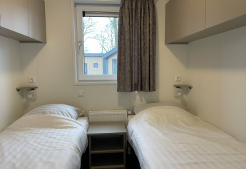 Due letti singoli in un Wood Cottage presso Holiday park De Witte Berg, Paesi Bassi, con finestra centrale.