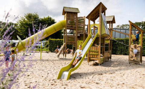 Niños jugando en un parque infantil con tobogán en Wood Cottage, Holiday park De Witte Berg, Países Bajos.
