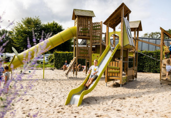 Kinder spielen auf einem Spielplatz mit Rutsche bei Wood Cottage im Ferienpark De Witte Berg, Niederlande.