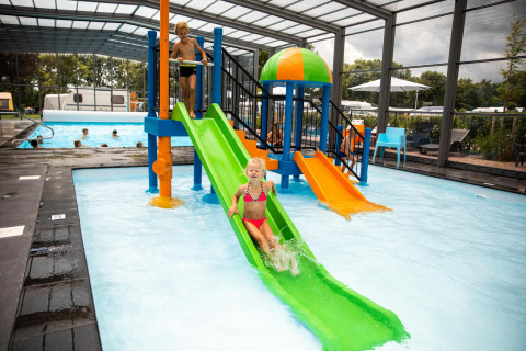 Kinderen glijden van kleurrijke waterglijbanen in een overdekt zwembad op een glampinglocatie.