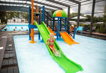 Children play on colorful water slides in an indoor pool area at a glamping accommodation in summer.